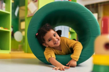 Child playing joyfully in a colorful daycare environment, crawling through a green tunnel, promoting active learning and engagement at Luv-N-Care Learning Center.